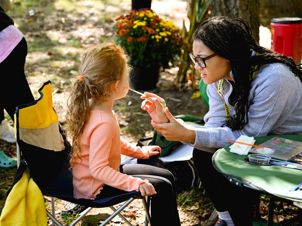 An artist painting a young visitor's face at Pond Fest