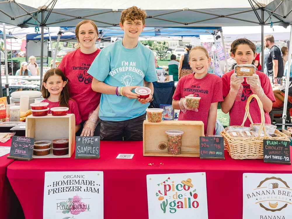 Young sellers behind a Kids Market booth of homemade jam and baked goods